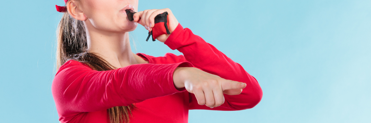 Office Halloween Costume. A woman weaing a red lifeguard shirt is blowing a whistle and pointing at the camera.