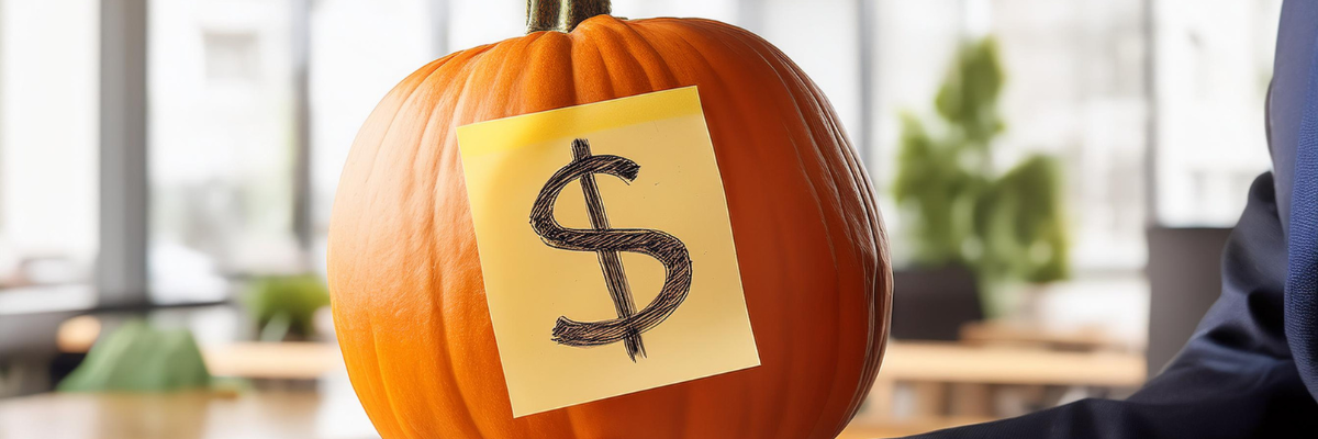 Office Halloween Costume. Someone is holding up a pumpkin with a sticky note that has a dollar sign marked on it. The background is a slightly blurred office setting.