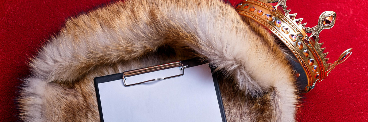 Office Halloween Costume. A crown, clipboard, and a furred cape are lying scattered on a red carpeted floor. The camera is looking at these objects from above.